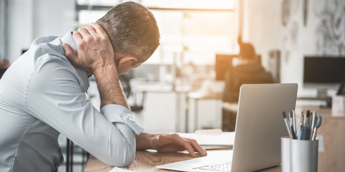 Man holding sore neck while using notebook computer. He sitting at table. Sick worker concept