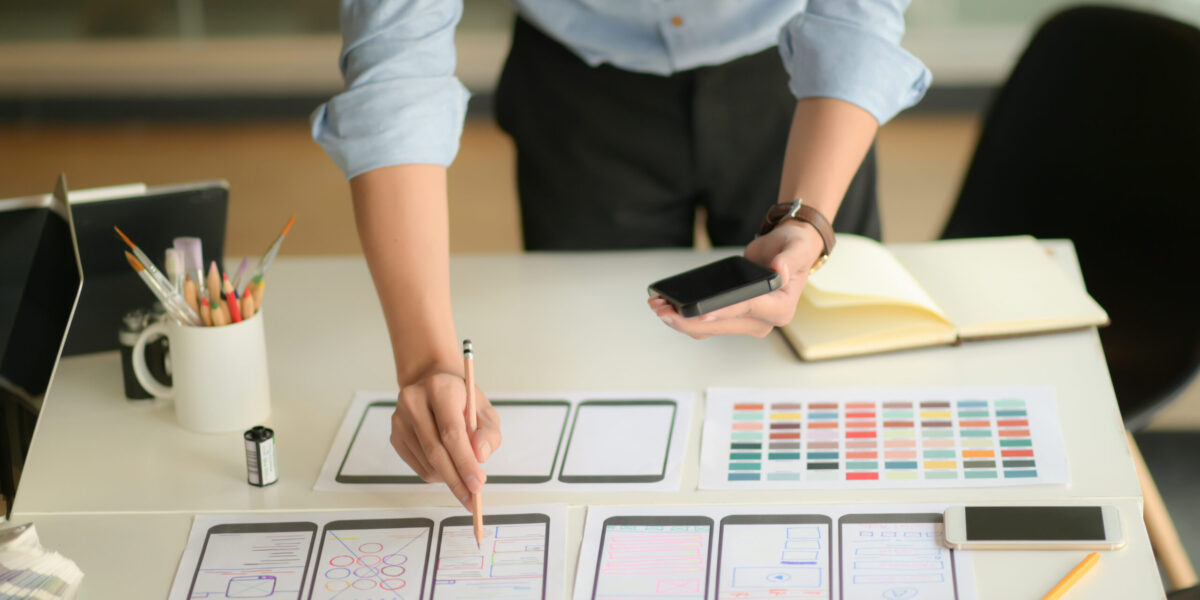 Cropped shot of young ux designer working on new application project while using smartphone in modern office room.