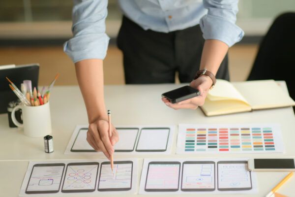 Cropped shot of young ux designer working on new application project while using smartphone in modern office room.